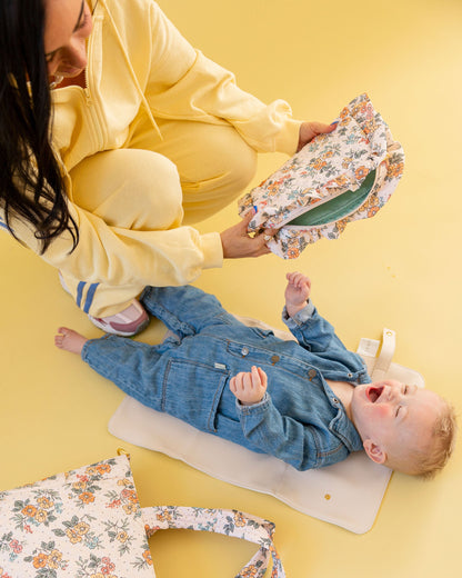Woman holding a floral-patterned bag next to a baby lying on a yellow floor.