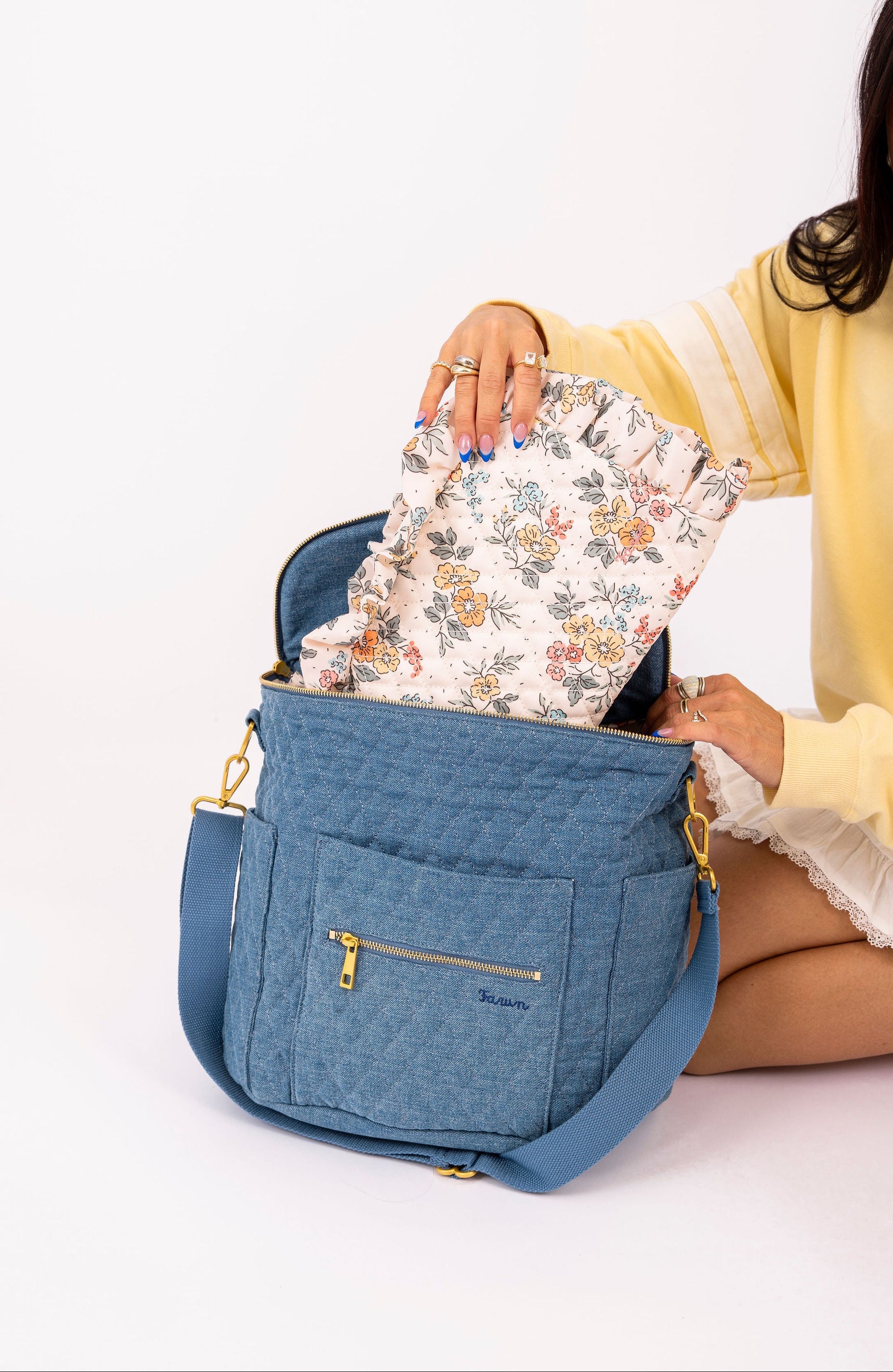 Woman holding a denim bag with a floral item inside on a white background