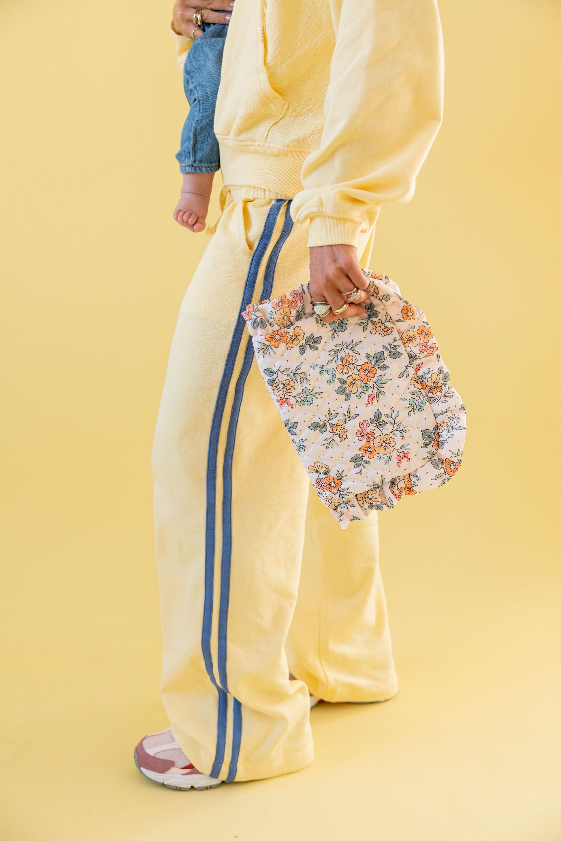 Person wearing a yellow outfit with blue stripes holding a floral clutch against a yellow background