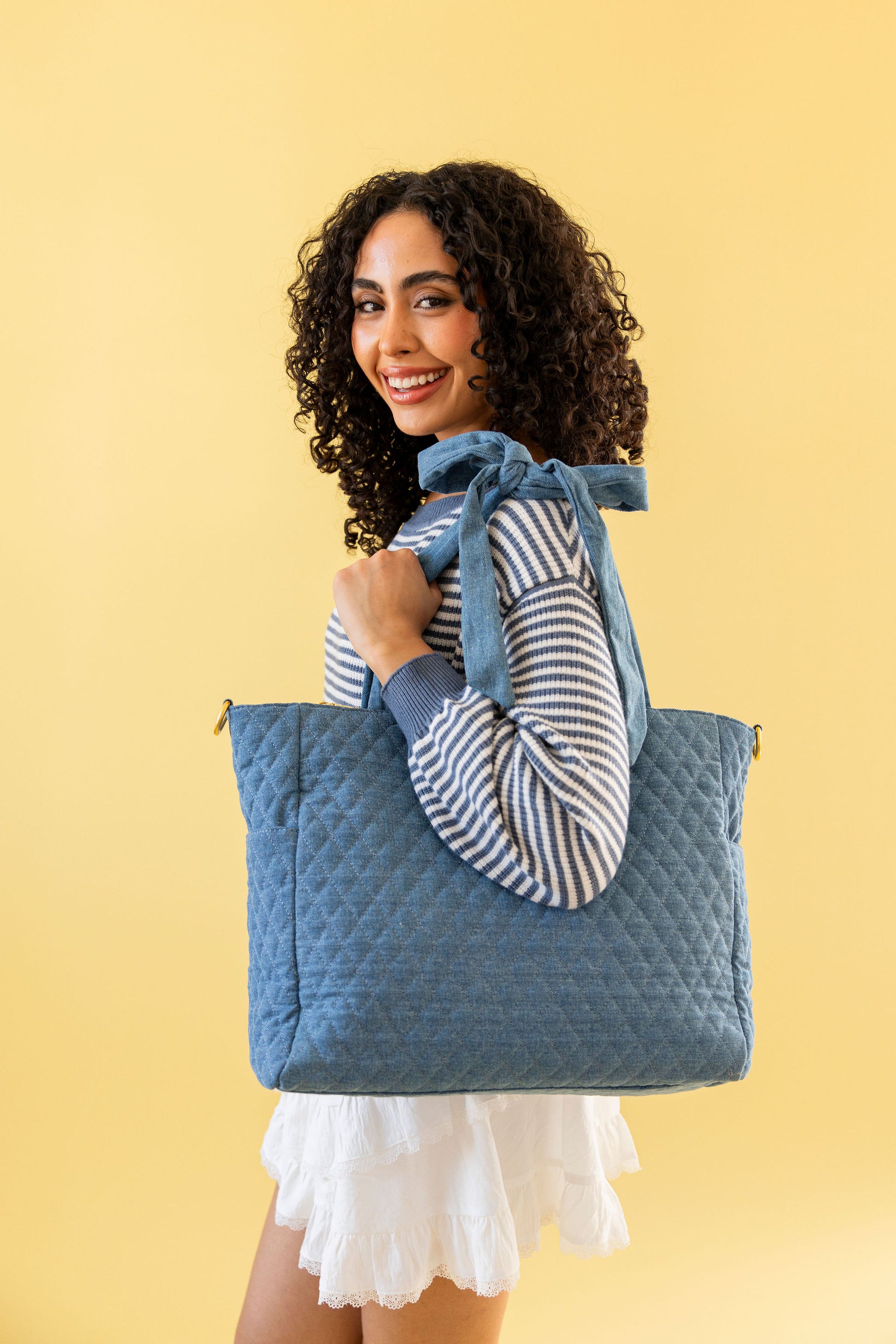 Woman holding a denim quilted tote bag against a yellow background