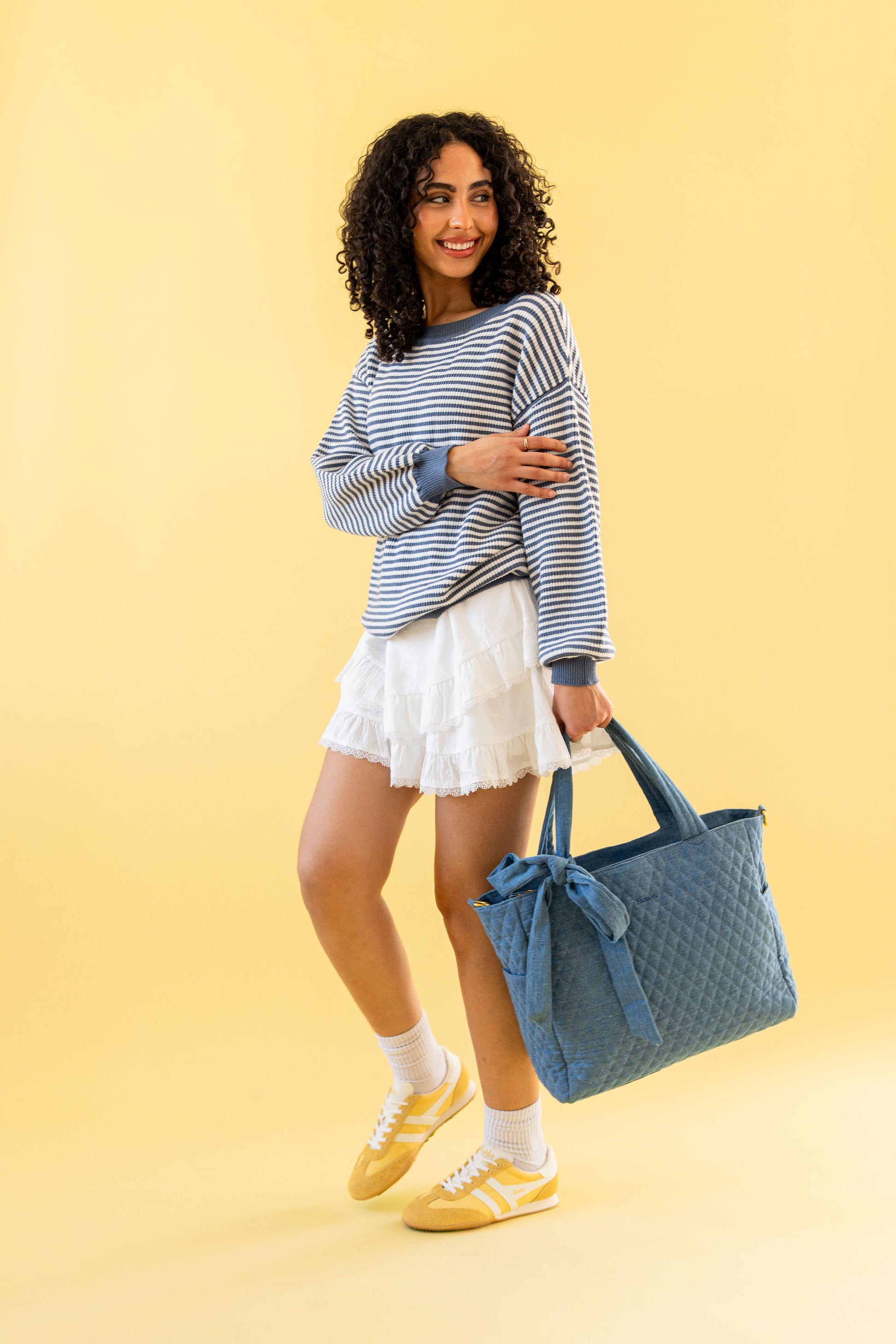 Woman holding a denim quilted bag against a yellow background