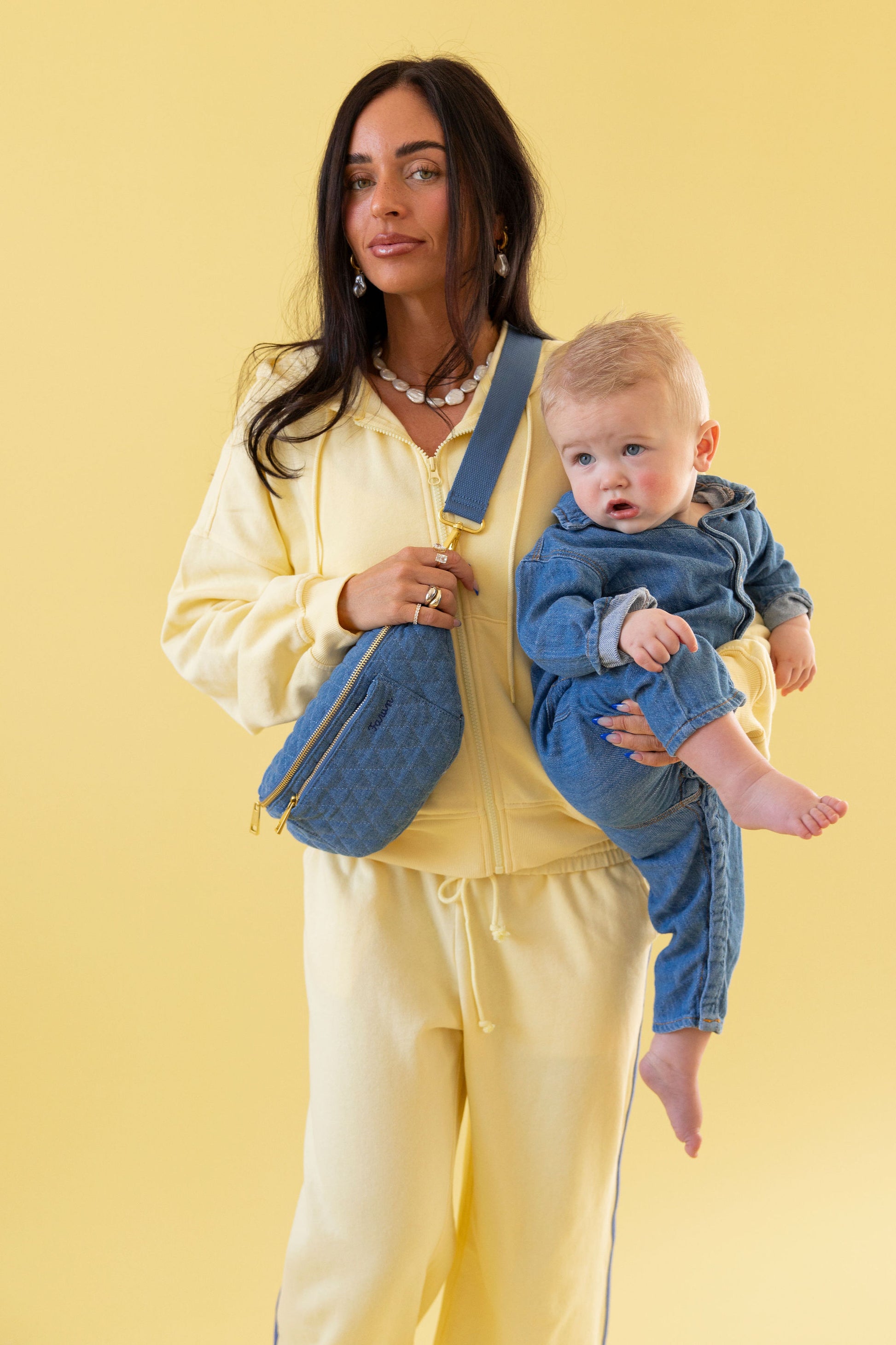 Woman holding a baby and wearing a fawny pack against a yellow background