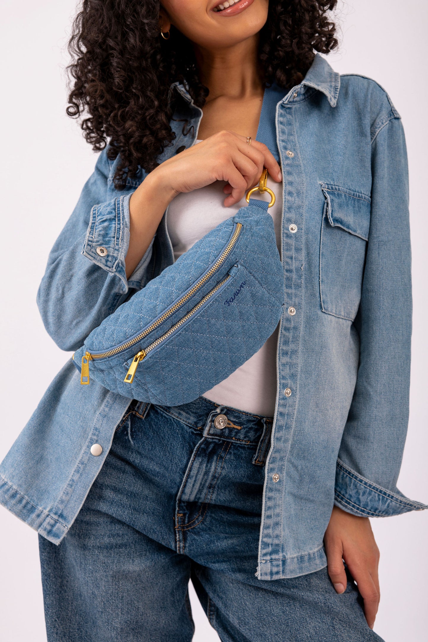Person wearing a denim jacket and jeans with a blue fawny pack on a white background