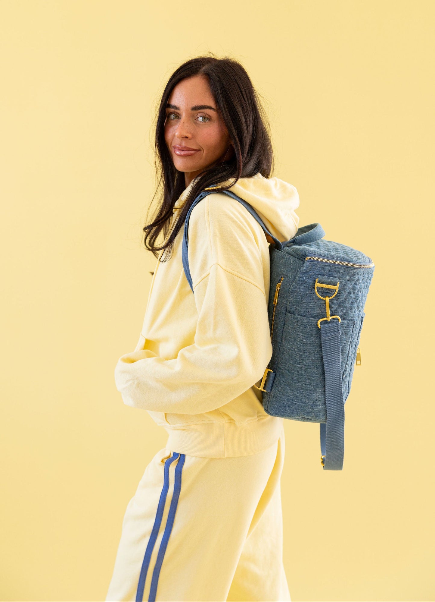 Woman in a yellow tracksuit with a blue backpack on a yellow background